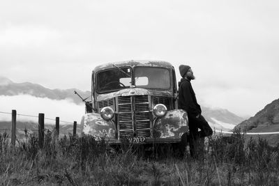 Man leaning against abandoned truck on field