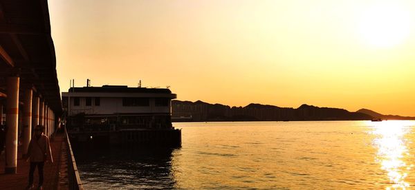 Silhouette buildings by sea against sky during sunset
