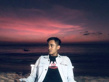 Young man standing in sea against sky during sunset