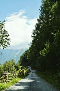 Empty road by trees on mountain against sky