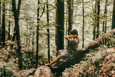 Side view of woman sitting on tree trunk in forest