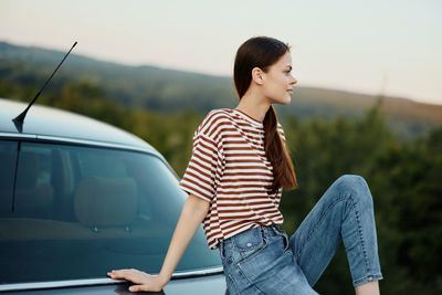 Side view of young woman standing against car