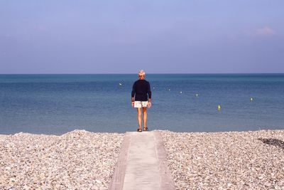 Rear view of senior man walking on footpath amidst pebbles at beach against sky
