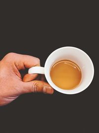 Close-up of hand holding coffee cup against black background