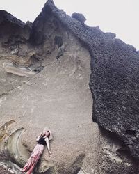 Midsection of woman on rock at beach against sky