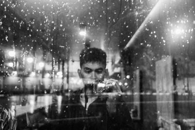 Portrait of man looking through wet window
