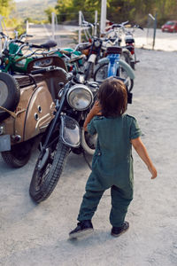 Child boy in a green jumpsuit walks among old motorcycles in the summer