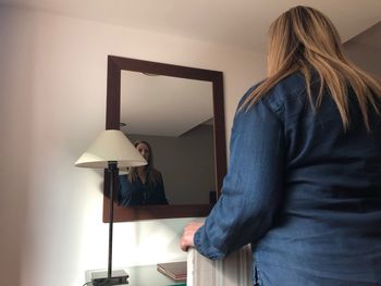 Rear view of woman standing against illuminated wall at home