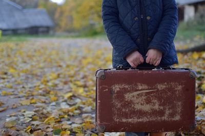 Midsection of child holding old luggage while standing on field during autumn