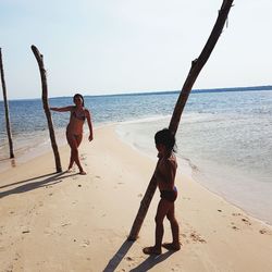 Mid adult woman with daughter standing at beach during sunny day