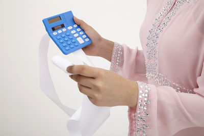 Midsection of woman holding receipt and calculator against white background