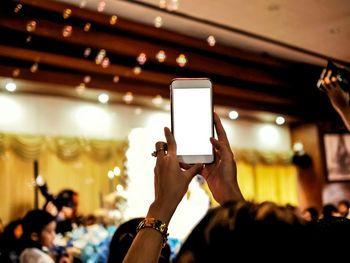 Cropped hands of woman using smart phone in illuminated room