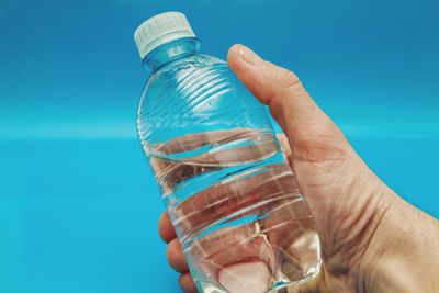 Close-up of hand holding glass bottle against blue water