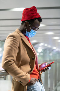 Side view of man wearing mask using phone while standing at airport