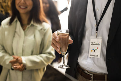 Midsection of businessman with wineglass standing by female colleague during corporate event