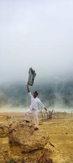 Person standing on land against sky during foggy weather