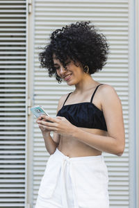 Young woman using mobile phone while standing against wall