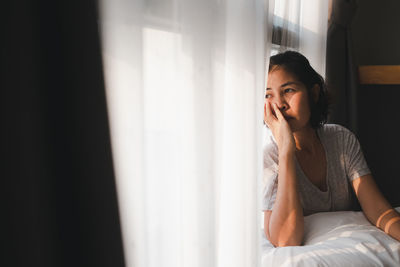 Young woman looking away while relaxing on bed at home