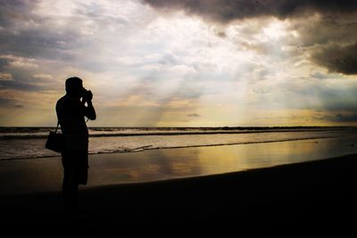 Silhouette man standing on beach against sky during sunset