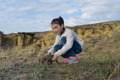 Cute girl holding tortoise against sky