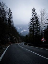 Road sign by trees against sky