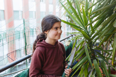 Half waist portrait of girl with dark hair taking care of the plants at the balcony