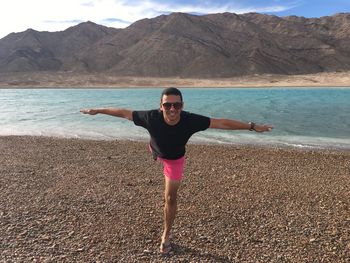 Full length portrait of man practicing yoga at lakeshore against mountains