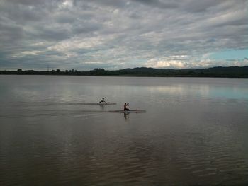 Men rowing boats in lake against cloudy sky