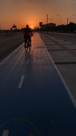 Man riding bicycle on road against sky during sunset