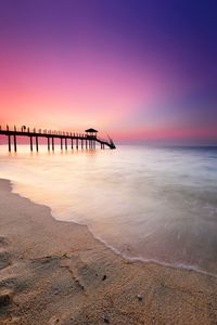 Silhouette jetty over sea against sky during sunset at penang