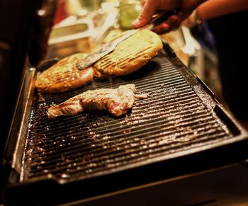 Cropped hand grilling meat on barbecue