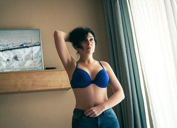 Woman in lingerie standing against wall at home