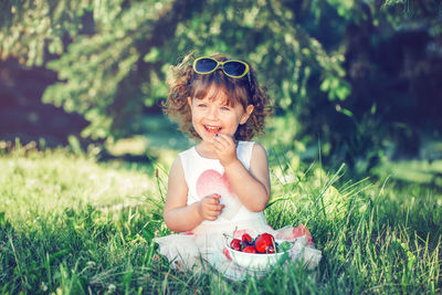 Smiling girl eating fruits in bowl while sitting on grass