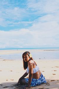 Young woman sitting on shore at beach against sky