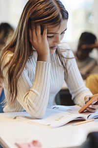 Sad girl with head in hand using mobile phone at desk