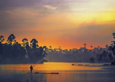 Silhouette fisherman fishing in lake against sky during sunrise