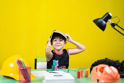 Portrait of smiling boy on table against yellow wall