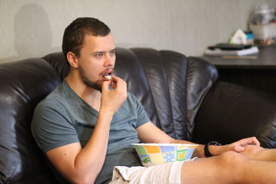 Young man looking away while sitting on sofa at home