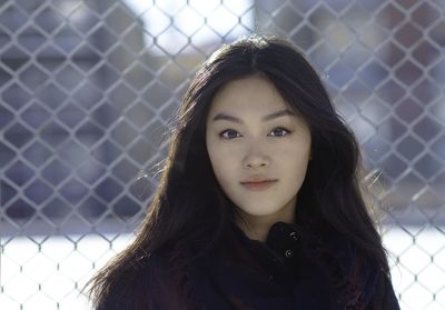 Portrait of young woman standing against chainlink fence