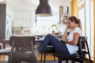 Side view of woman watching digital tablet while sitting on chair at home