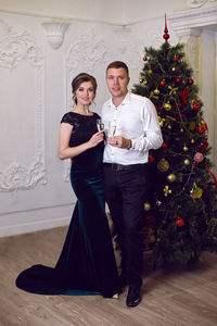 Woman in a dress with a man in a suit holding champagne at the christmas tree on christmas day