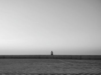 Man sitting alone on sea against clear sky