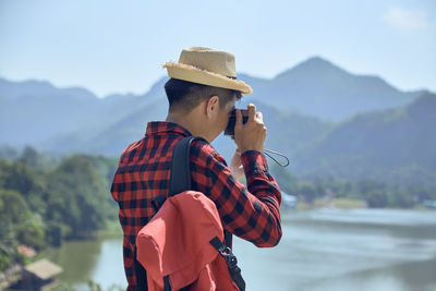 Man holding hat standing against mountain range