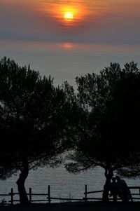 Silhouette men by sea against sky during sunset