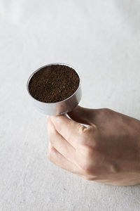 Cropped image of hand holding ground coffee in container at table