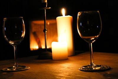 Illuminated candles by wineglass on table in darkroom