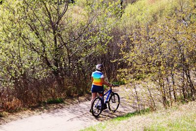 Rear view of woman walking with bicycle on road amidst trees