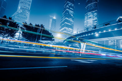 Light trails on road by illuminated buildings in city at night