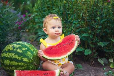 Cute girl eating watermelon sitting against plants