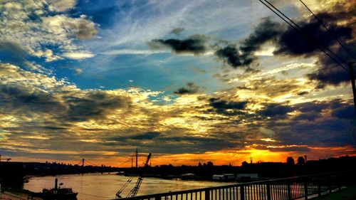 Silhouette bridge over river against dramatic sky